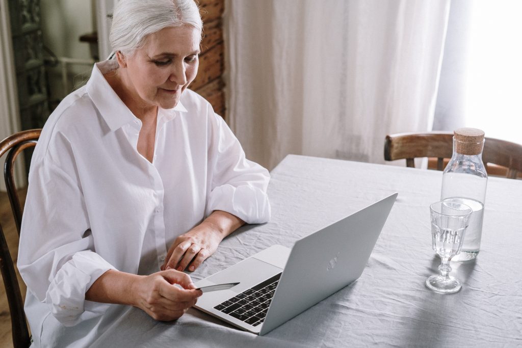 Photo of elderly woman looking at card in front of laptop