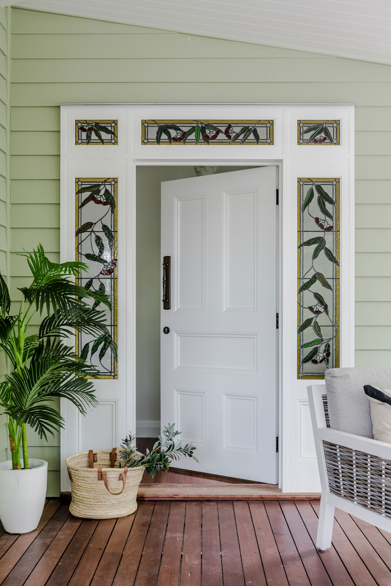 An white front door open to the interior of a home. Surrounding the door are potted plants and green cladding.